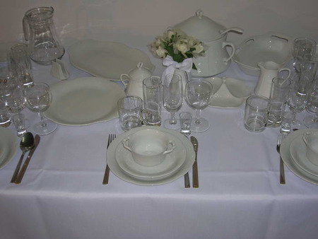 Elegancko nakryty stół z białą zastawą stołową i bukietem białych kwiatów, przygotowany do uroczystego przyjęcia.